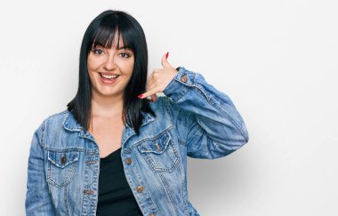 Gündelik kıyafetler giymiş, gülümseyen, el ve parmaklarıyla telefon hareketi yapan, telefonda konuşur gibi genç İspanyol bir kadın. iletişim kavramları. 