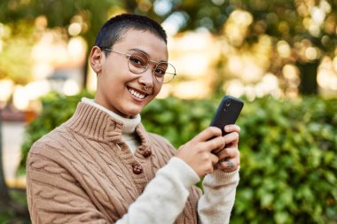Kısa saçlı genç İspanyol kadın akıllı telefon kullanarak mutlu bir şekilde gülümsüyor.