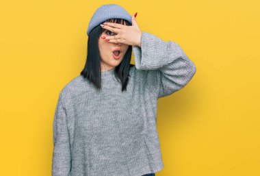 Şirin yün şapka takan genç İspanyol kadın şok içinde yüzünü ve gözlerini kapayarak utangaç ifadesiyle parmaklarının arasından bakıyor.. 