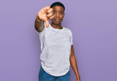 Genç Afro-Amerikalı kadın, gündelik beyaz tişört giyiyor mutsuz ve kızgın görünüyor, reddediliyor ve olumsuz jestler yapıyor. kötü ifade. 