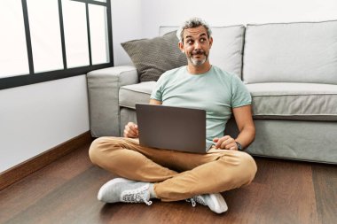 Orta yaşlı İspanyol adam dizüstü bilgisayar kullanıyor oturma odasında oturmuş gülümsüyor yan bakıyor ve düşünüyor.. 