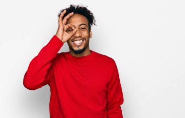 Sakallı, kışlık süveter giyen, el hareketleriyle gülümseyen, mutlu yüzüyle parmaklarının arasından bakan Afro-Amerikalı genç bir adam.. 