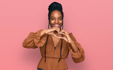Genç Afro-Amerikan kadın, günlük kıyafetler giyip, aşıkken gülümsüyor, elleriyle kalp sembolü yapıyor. romantik kavram. 