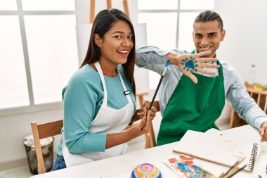 Genç Latin ressam çift gülümsüyor resim stüdyosunun masasında mutlu bir resim çiziyor.
