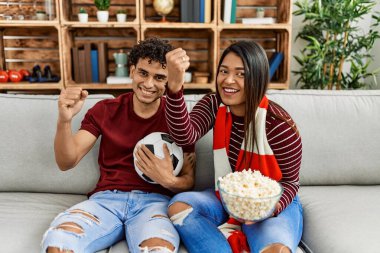 Evdeki kanepede oturan genç latin çift futbol maçını izliyor ve destekliyor..