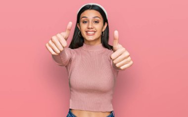 Latin asıllı genç bir kız günlük giysiler giyip olumlu jestler yapıyor. Elleriyle gülümsüyor ve başarı için seviniyor. kazanan jest. 