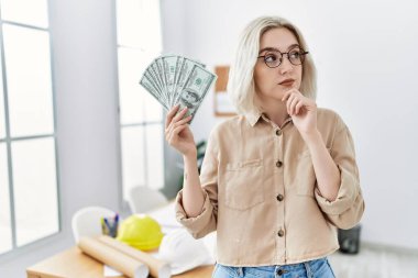 İnşaat ofisindeki genç, beyaz bir kadın elinde para, ciddi bir yüz ifadesi var. Çene ve çeneyle soru sormayı düşünüyor. Kafa karıştırıcı bir fikir. 