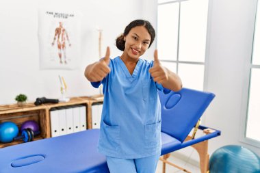 Ağrı kesici kliniğindeki güzel İspanyol fizyoterapist kadın elleriyle olumlu jest yapmayı onaylıyor, gülümsüyor ve başarı için mutlu. kazanan jest. 