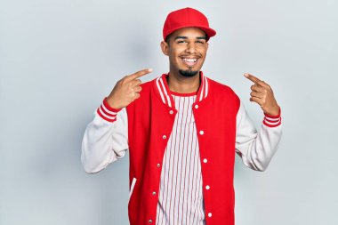 Beyzbol üniforması giyen, gülümseyen, parmaklarını ve ağzını gösteren Afro-Amerikan genç adam. diş sağlığı kavramı. 