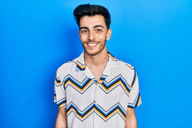 Yüzünde mutlu ve havalı bir gülümseme olan sıradan kıyafetler giyen genç İspanyol bir adam. şanslı kişi. 