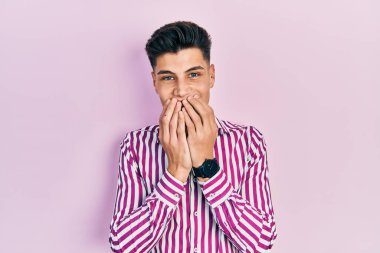 Günlük kıyafetler giyen genç İspanyol adam gülüyor ve utanıyor kıkır kıkır kıkır gülüyor elleriyle ağzını kapatıyor, dedikodu ve skandal konsepti. 