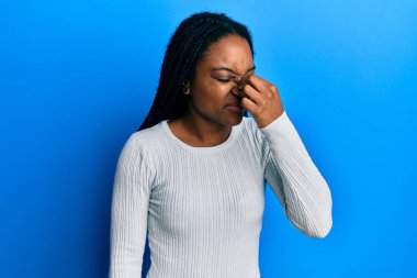 Saçları örgülü, günlük beyaz süveter giyen, burnu ve gözleri ovuşturan yorgun ve başı ağrıyan Afro-Amerikalı bir kadın. Stres ve hüsran kavramı. 