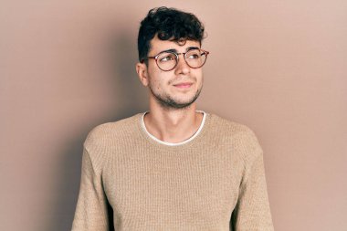 Gündelik kıyafetler ve gözlük takan genç İspanyol adam gülümseyip yan tarafa bakıyor ve düşünüyor.. 