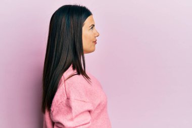 Güzel esmer kadın, günlük kışlık süveter giyiyor. Yan tarafa bakıyor, rahat bir poz veriyor. Kendine güvenen bir gülümsemesi var.. 