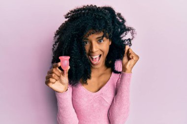 Afro saçı olan Afrikalı bir kadın elinde fincanla gururla bağırıyor zaferi ve başarıyı kutluyor. Kollarını kaldırarak heyecanlanıyor. 