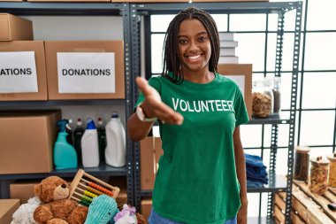 Bağışlarda gönüllü tişört giyen Afro-Amerikalı genç bir kadın karşılama ve hoş geldin demek için gülümseyerek el sıkışır. başarılı iş. 
