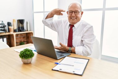 Ofiste çalışan kıdemli bir adam bilgisayarla el hareketleriyle büyük boyut ve ölçü sembolü gösteriyor. Kameraya bakıp gülümsüyor. ölçüm kavramı. 