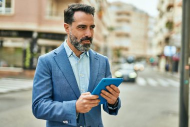 Orta yaşlı işadamı şehirde dokunmatik ped kullanarak mutlu bir şekilde gülümsüyor..