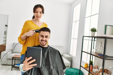 Kuaför kadın güzellik merkezinde saç keserken genç İspanyol adam perdeye bakıyor..