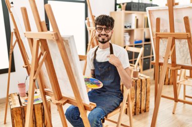 Sanat stüdyosunda sakallı bir İspanyol mutlu ve gururlu birini işaret ediyor. 