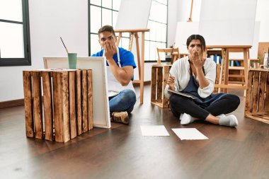 Sanat stüdyosundaki genç İspanyol çift ağızlarını eliyle kapatıyor, şaşırıyorlar ve hata yapmaktan korkuyorlar. şaşırmış ifade 