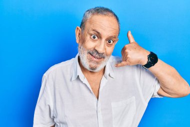 Sakallı, sıradan beyaz tişörtlü, yakışıklı, telefonda el ve parmak hareketleriyle gülümseyen, telefonda konuşan bir adam. iletişim kavramları. 