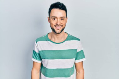 Yüzünde mutlu ve havalı bir gülümseme olan sıradan kıyafetler giyen genç İspanyol bir adam. şanslı kişi. 