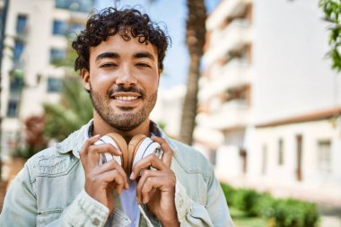 Yakışıklı, sakallı, neşeli, güneşli bir günde kulaklık takan bir İspanyol.