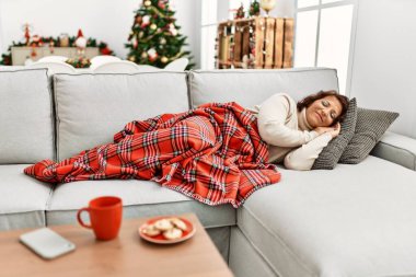 Orta yaşlı İspanyol kadın evdeki Noel ağacının yanında kanepede uyuyor..