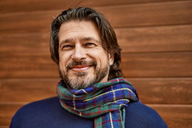 Duvara yaslanmış gülümseyen orta yaşlı yakışıklı adam.