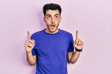 Gündelik tişört giyen genç İspanyol adam şaşırmış ve şaşırmış bir şekilde yukarı baktı ve parmaklarıyla işaret etti ve kollarını kaldırdı.. 