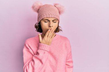 Şirin yün şapka takan esmer, esnemekten sıkılmış, ağzı eliyle kapatan genç bir kadın. Huzursuz ve uykulu.. 