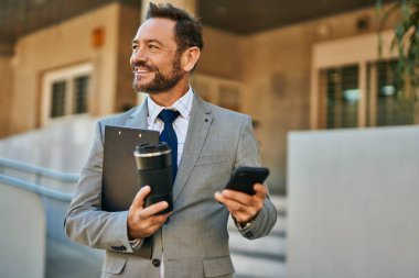 Orta yaşlı işadamı akıllı telefon kullanıyor ve şehirde kahve içiyor..