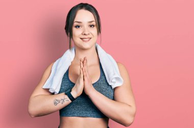 Spor kıyafetleri giymiş, havluyla birlikte dua eden genç İspanyol kız af diliyor kendinden emin bir şekilde gülümsüyor.. 