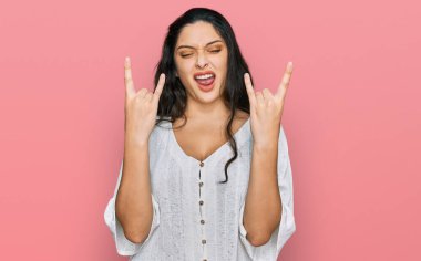 Esmer, gündelik giysiler içinde çılgın bir ifadeyle bağıran genç bir kadın elleri havada rock sembolü yapıyor. Müzik yıldızı. ağır kavram. 