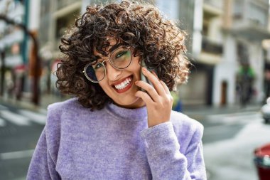 Orta Doğulu genç bir kadın gülümsüyor. Akıllı telefondan konuşuyor.