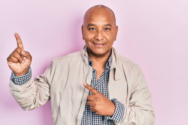 Orta yaşlı, sıradan kıyafetler giyen, gülümseyen ve kameraya bakan, iki eli ve parmakları yanda olan Latin bir adam.. 