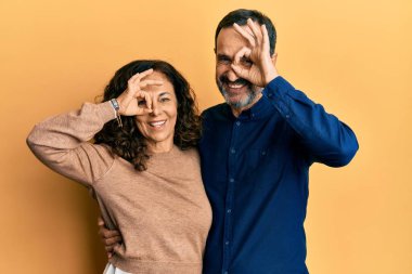 Orta yaşlı İspanyol çift gündelik kıyafetler giyip el hareketleriyle gülümsüyor ve mutlu yüzleriyle parmaklarının arasından bakıyor.. 