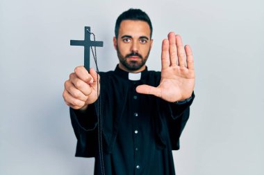 Sakallı, elinde Katolik haçı olan yakışıklı bir İspanyol papaz dur işareti yapıyor ciddi ve kendinden emin bir ifadeyle, savunma jesti yapıyor. 