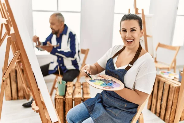 若いアーティストの女性とアートスタジオの教室でシニア画家の男性キャンバス上の絵画 アーティストパレットに油絵を注ぐ女性のクローズアップ — ストック写真
