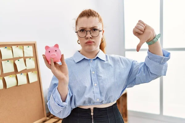 Jonge Roodharige Vrouw Houdt Varkensbank Kantoor Met Boos Gezicht Negatief — Stockfoto