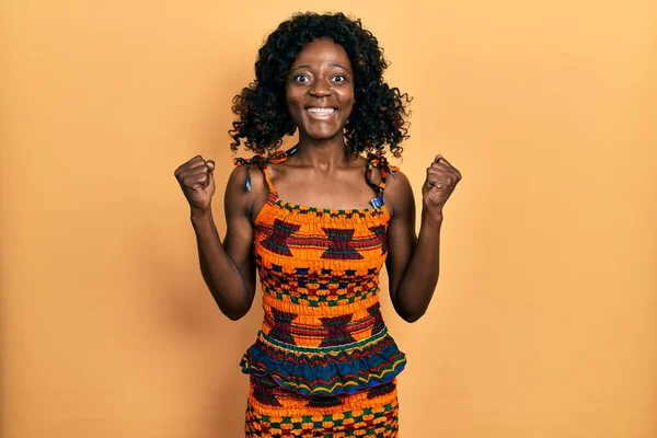 年轻的非洲裔美国女人穿着传统的非洲服装 以张开双臂和睁开眼睛庆祝成功 她对此感到惊讶和惊奇 获奖者概念 — 图库照片