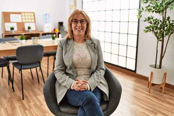 Middle age businesswoman smiling happy sitting with arms crossed gesture at the office.