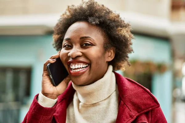 Beautiful business african american woman with afro hair smiling happy and confident outdoors at the city having a conversation speaking on the phone
