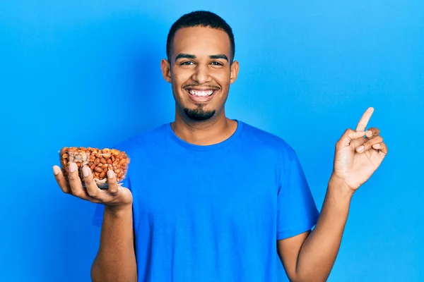Joven Hombre Afroamericano Sosteniendo Tazón Cacahuetes Sonriendo Feliz Señalando Con — Foto de Stock