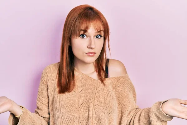 红头发的年轻女子穿着休闲的冬季毛衣 毫无头绪 满脸困惑 手臂和双手高举 怀疑概念 — 图库照片