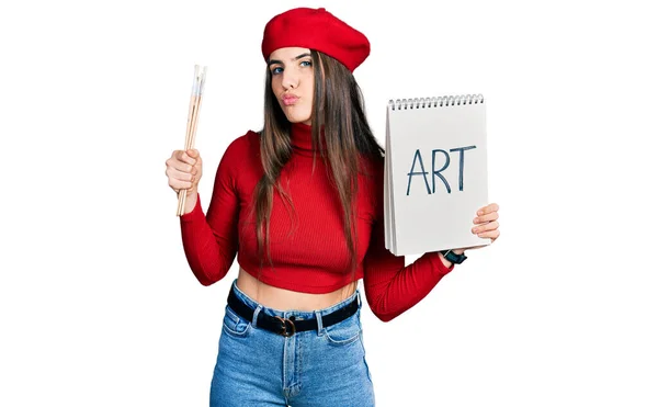 Young Brunette Teenager Holding Art Notebook Paintbrushes Looking Camera Blowing — Stock Photo, Image
