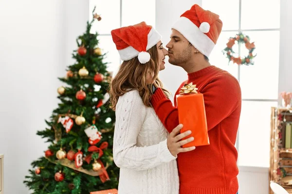 Young Hispanic Couple Wearing Christmas Hat Holding Gift Home — Stock Photo, Image
