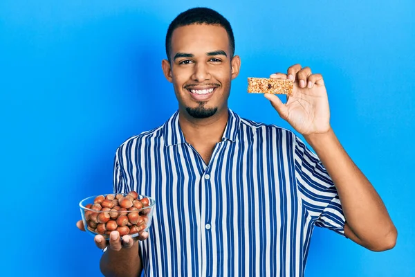 Joven Hombre Afroamericano Sosteniendo Avellanas Crudas Barra Cereales Sonriendo Con — Foto de Stock