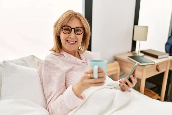 Orta Yaşlı Sarışın Kadın Yatakta Uzanıyor Akıllı Telefon Kullanıyor Evde — Stok fotoğraf